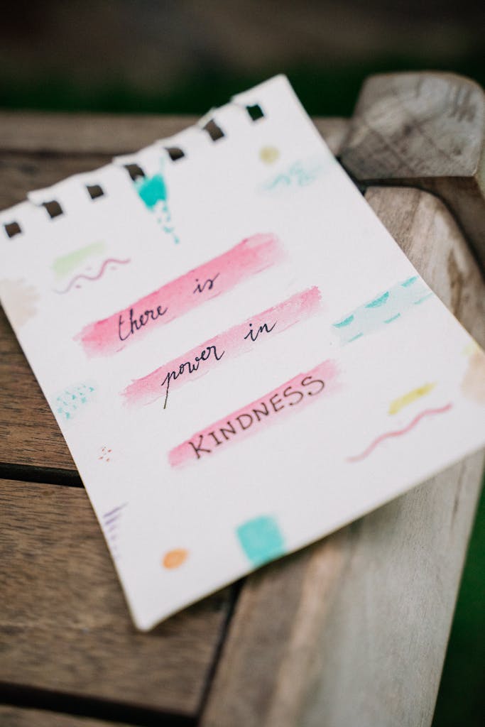 A handwritten note on a white paper with 'there is power in Kindness' against a wooden background.
