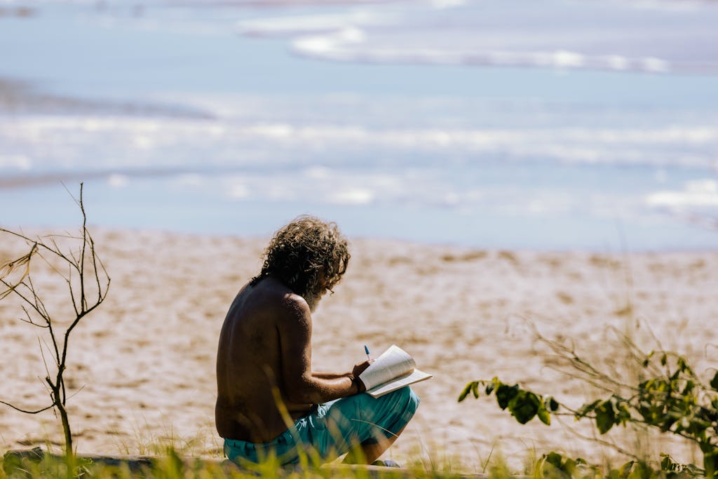 A man enjoying a quiet moment near the sea, writing in a notebook working on becoming aware on a sunny beach.